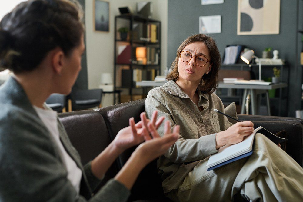 Two women sitting on couch discussing treatment plan during counseling session